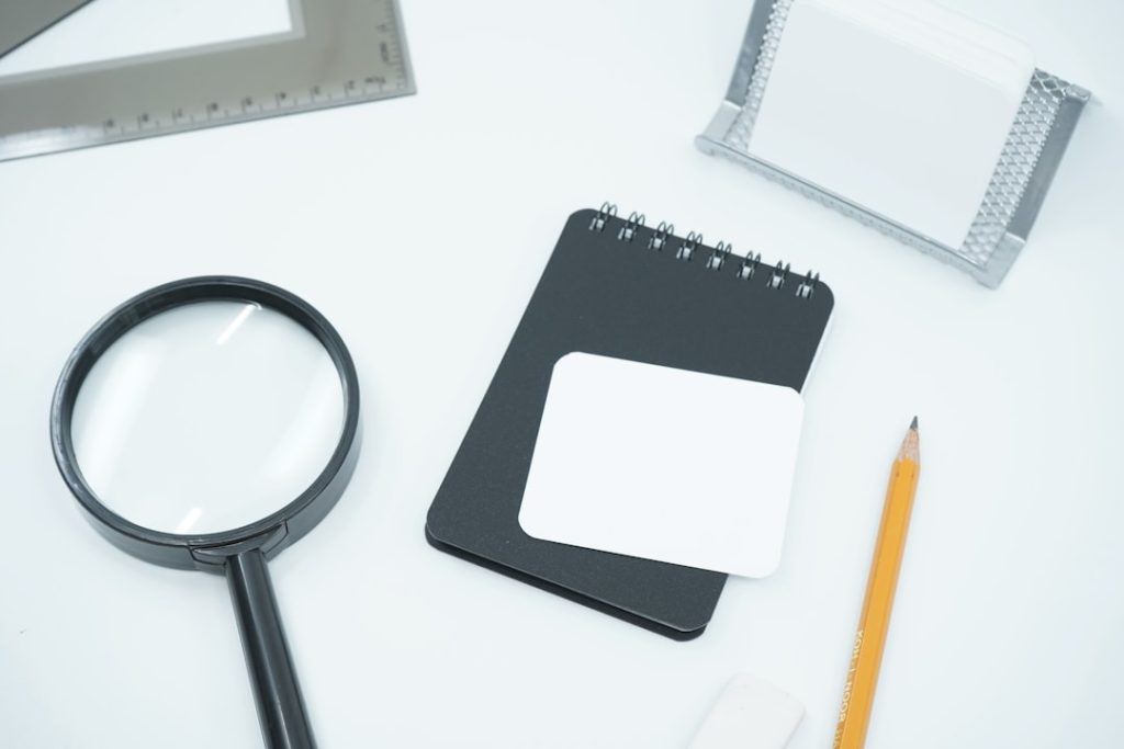 a magnifying glass, a notebook, and a pencil on a white surface